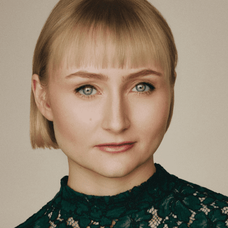 Rae Gray's Headshot, a blonde woman against a beige background